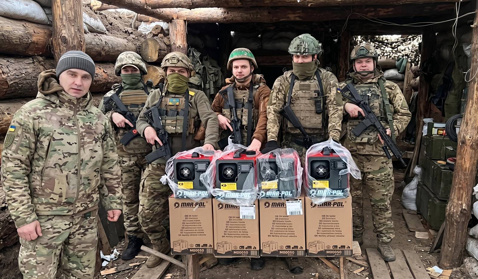 Soldiers of the 37th Marine Brigade standing in a log dugout behind four boxed diesel heaters